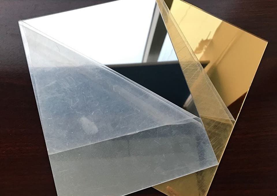 Plaques de PMMA miroir argent et or superposées, l'une encore recouverte de son film de protection.